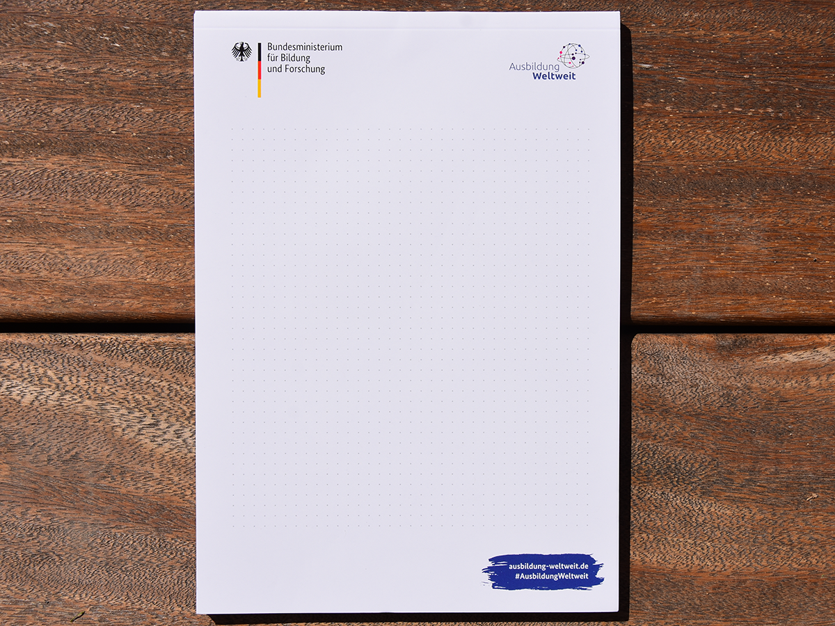 Schreibblock, bedruckt mit den Logos vom BMBF und von AusbildungWeltweit sowie URL ausbildung-weltweit.de und #AusbildungWeltweit auf blauem Hintergrund