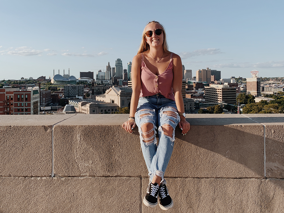 Leonie Petri sitzt auf einer Mauer vor der Skyline von Kansas City 