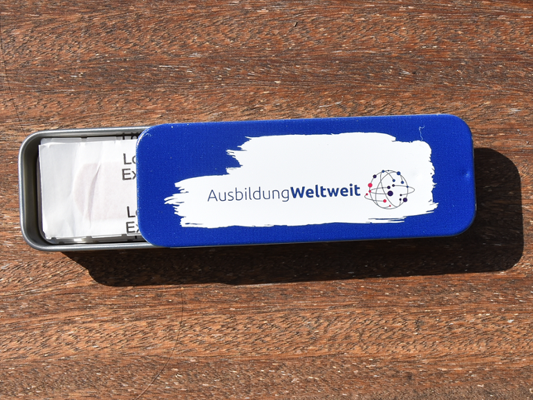 Pflasterset in metallener Box, blauer Hintergrund und Logo auf weiß