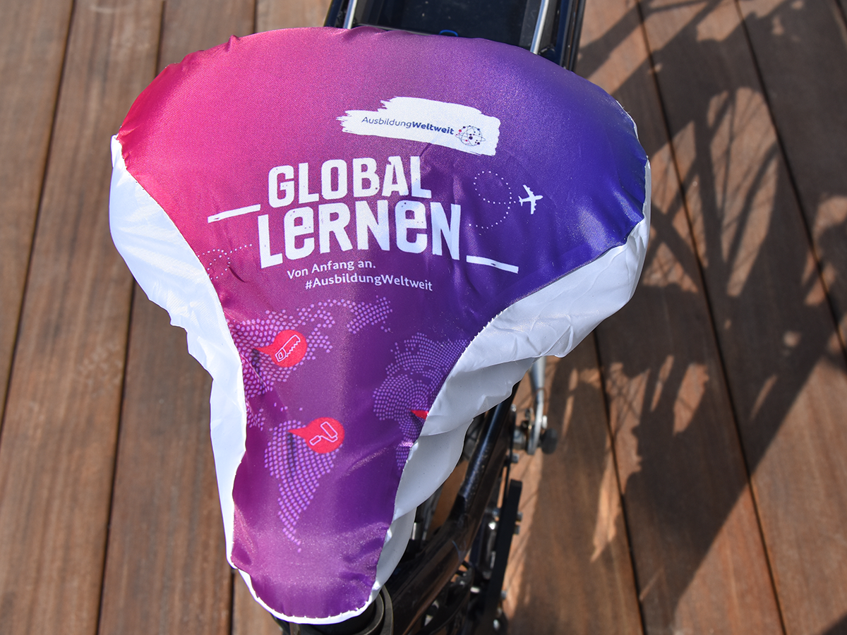 Sattelschutz in den Farben von AusbildungWeltweit mit Weltkarte und Schriftzug "Global lernen von Anfang an" und Logo