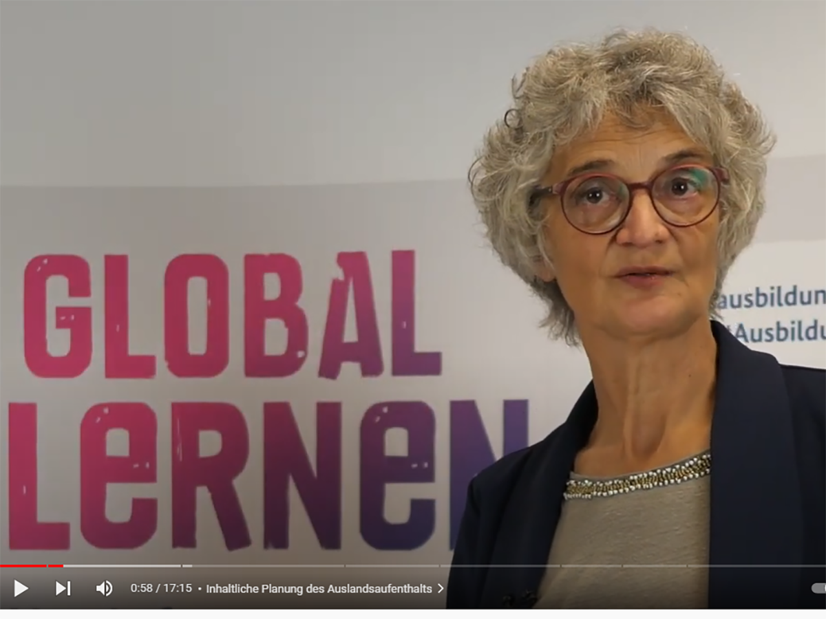 Screenshot aus dem Video: Susanne Timmermann vor Videohintergrund mit Kampagenenslogan: Global Lernen. 